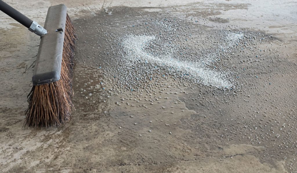 A straw-bristled broom and water cleans up an oil spill in a household garage with oil-absorbing cat box litter granules
