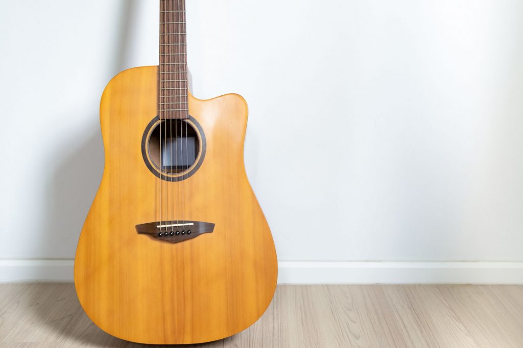 An acoustic dreadnought guitar leaned against the white wall of the room background