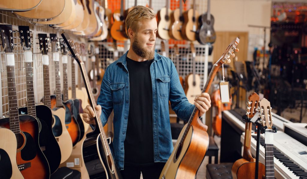 Young guy choosing acoustic guitar in music store
