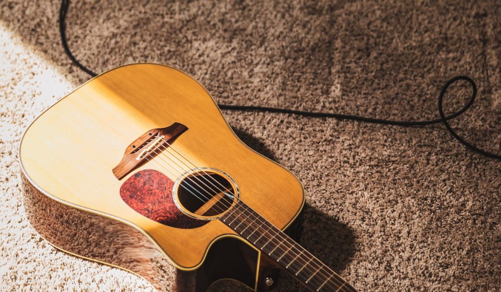 dreadnought acoustic guitar laying on carpet with sunlight hitting half of the guitar.