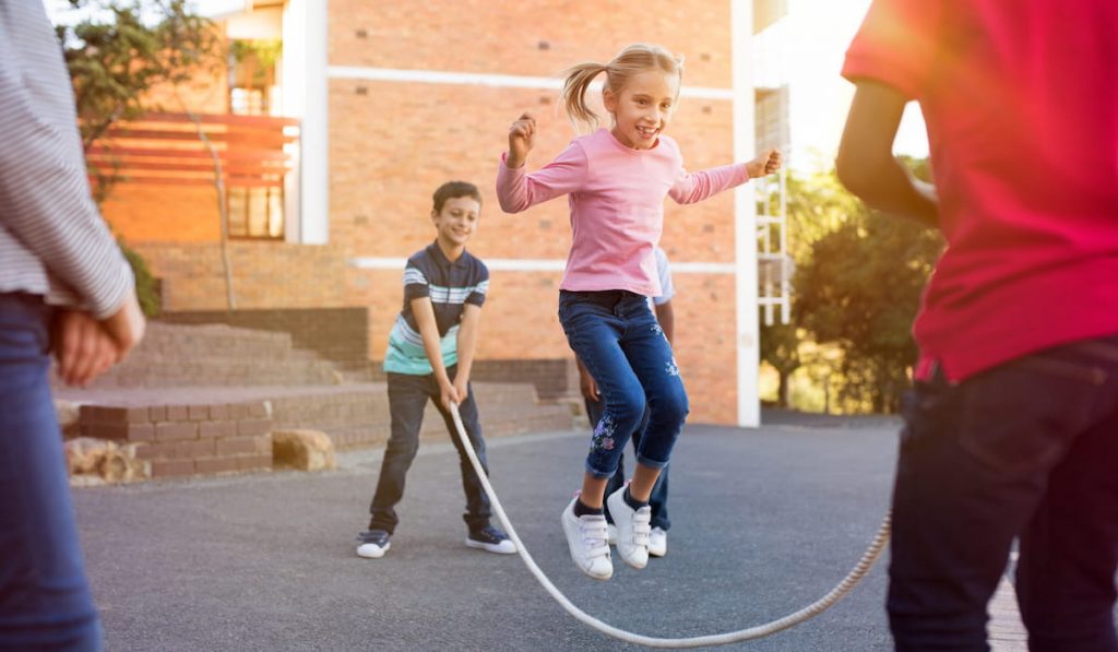 Happy elementary kids playing together with jumping rope outdoor
