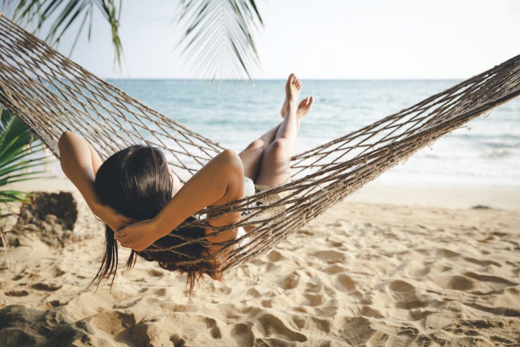  woman relaxing in hammock on tropical beach at sunset