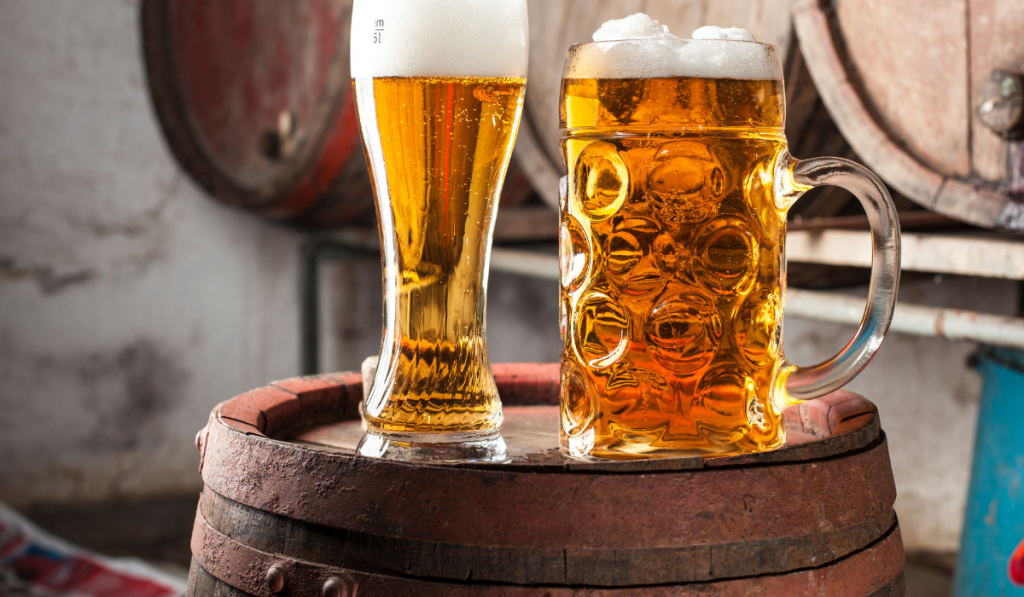 Two Beers with foam and old wood barrels in the background

