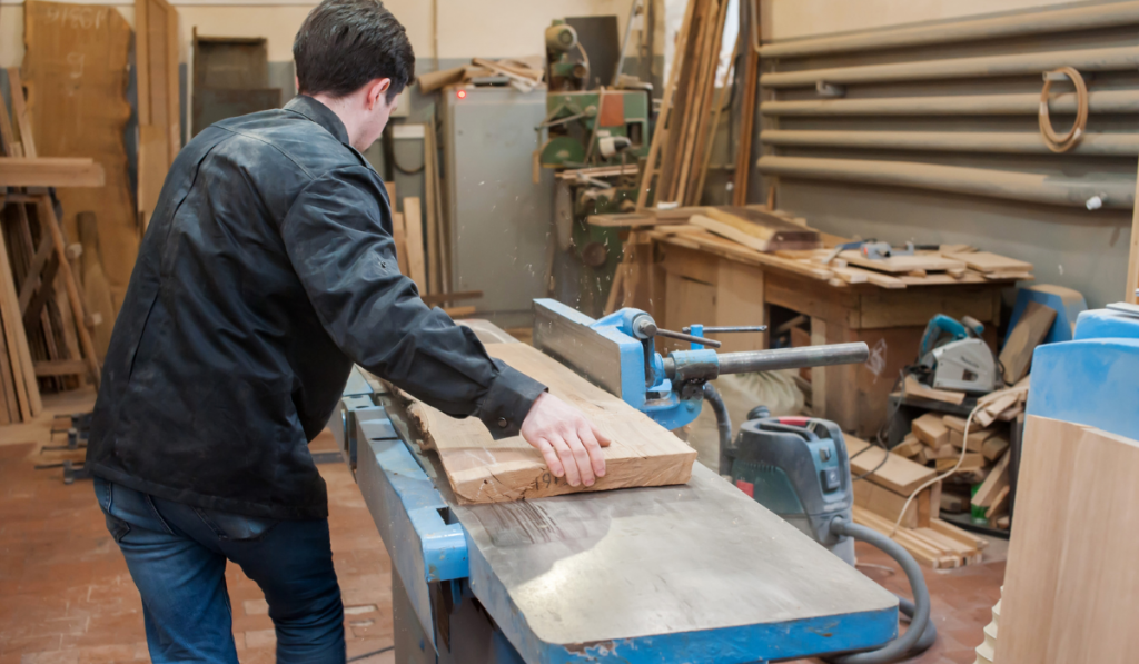 Male carpenter planning wood on a lathe in a carpentry workshop