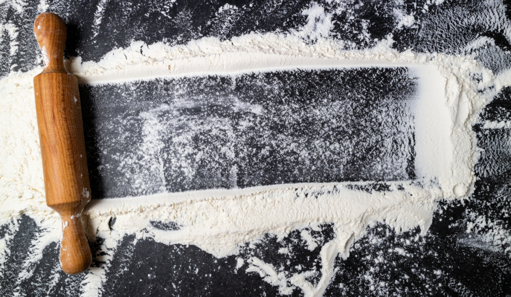 Rolling pin and white flour on dark table.