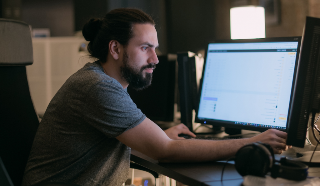 A young man plays video games in front of monitors in the evening.