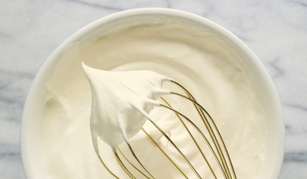 Gold whisk and homemade whipping cream on marble table