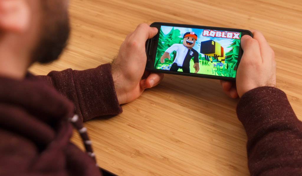 Man holding a smartphone and playng the Roblox mobile game.