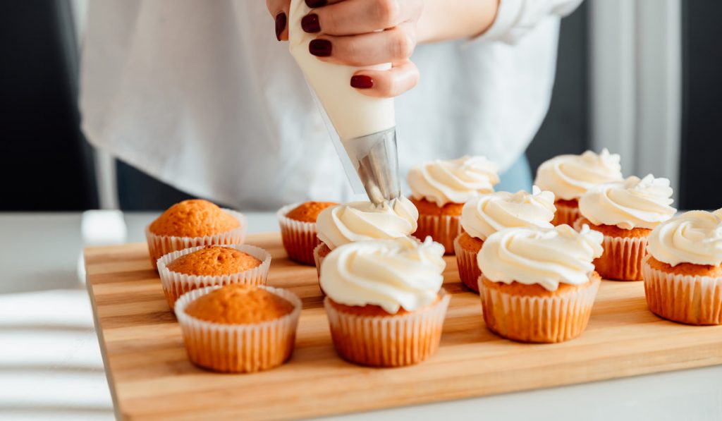 Woman decorates freshly baked cupcakes with whipped cream