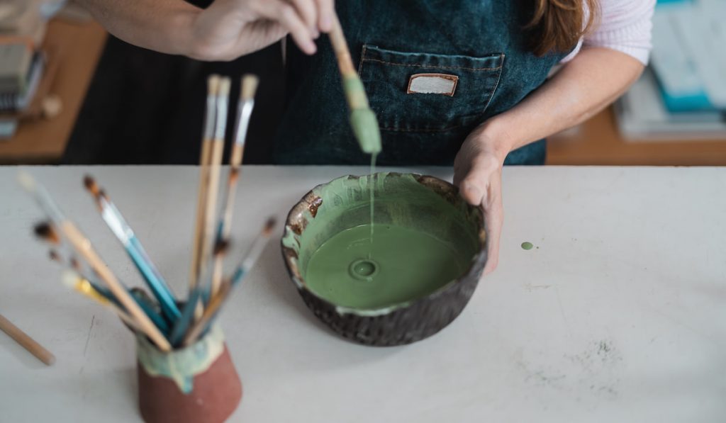 Woman mixing paint with brush inside ceramic bowl in workshop studio
