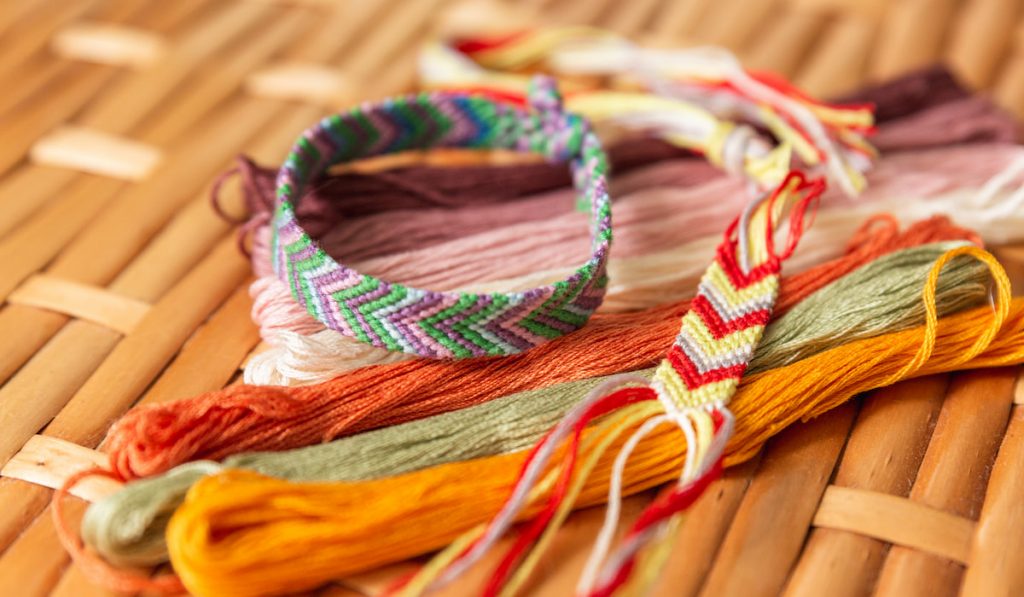 Woven bracelet made of bright cotton threads, colorful threads for embroidery on rattan table.
