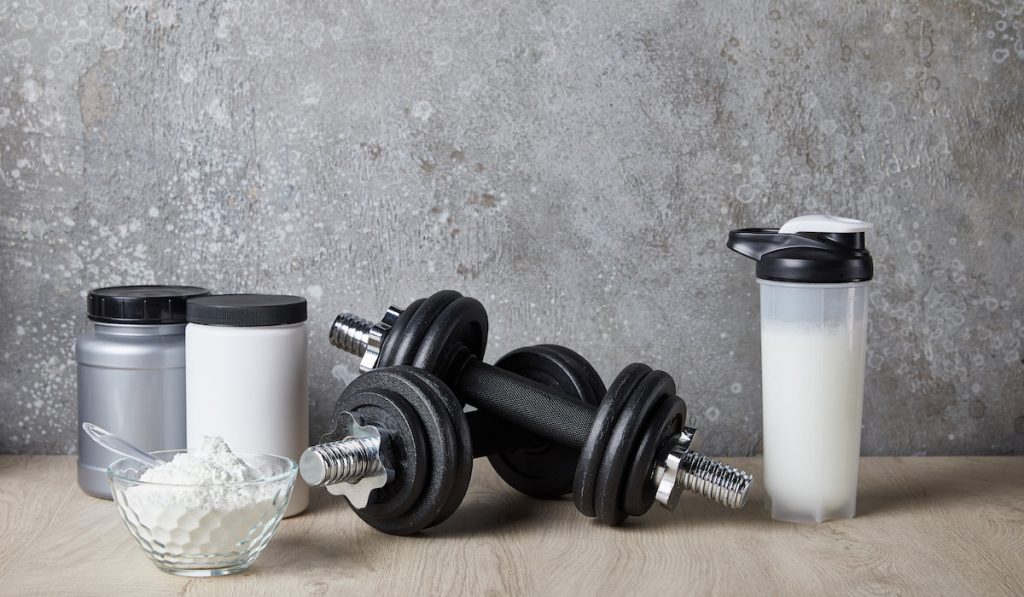 protein shake in sports bottle near jars and dumbells near concrete wall